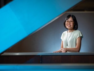 A female smiling and posing for a photo. Her hands are laying on a railing of some stairs.