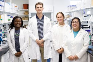 Three women and one man standing in a lab.