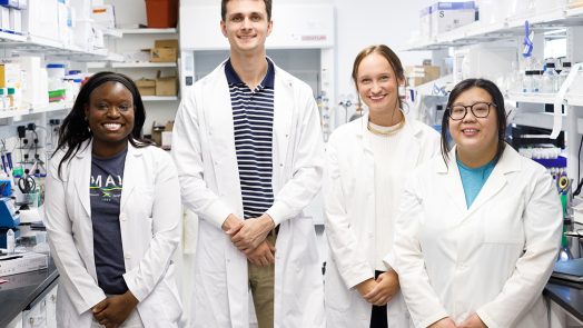 Three women and one man standing in a lab.