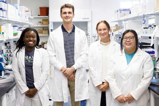 Three women and one man standing in a lab.