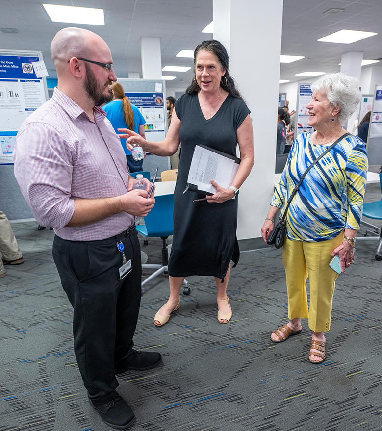 A man and two women holding papers and a phone converse.