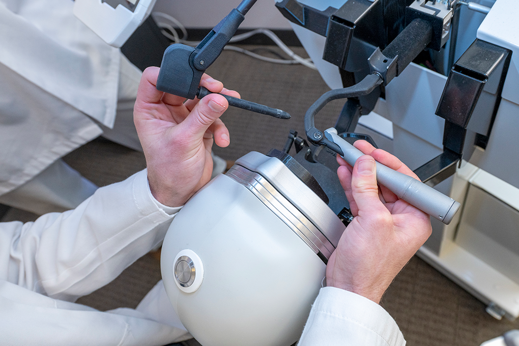 A pair of hands use an dental simulation tool to practice filling in a cavity.