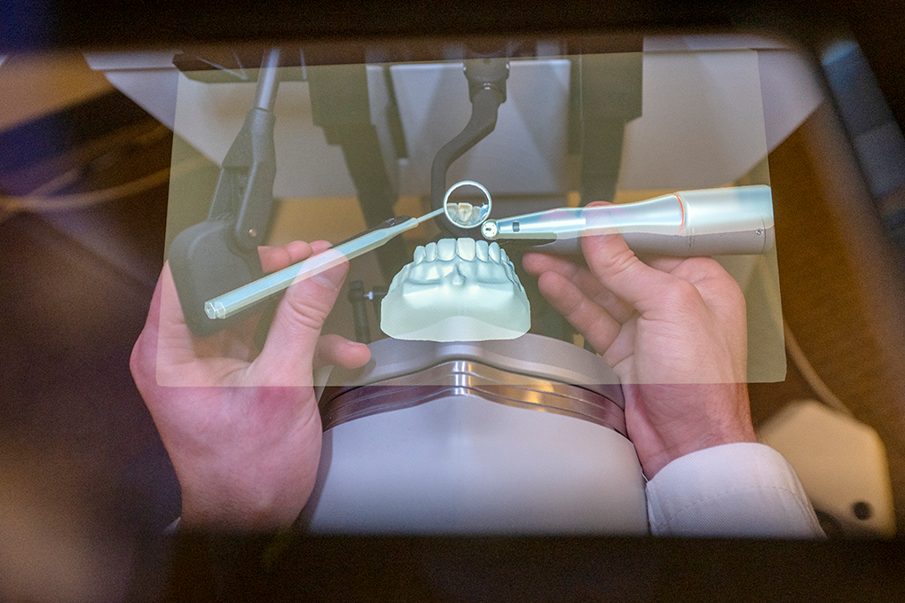 A pair of hands use an dental simulation tool to practice filling a cavity.