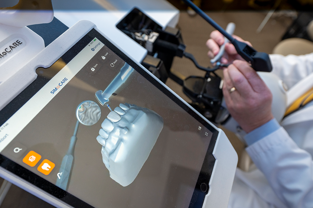 A close up of a mouth model shown on a dental simulation tool. A pair of hands use the tool in the background.