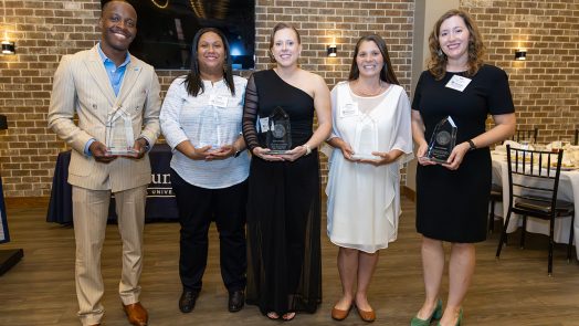Smiling people holding award statues