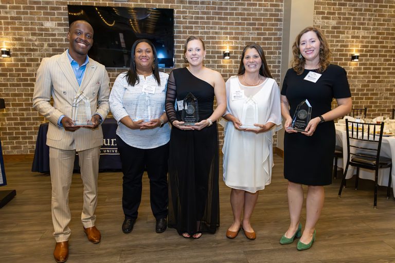 Smiling people holding award statues