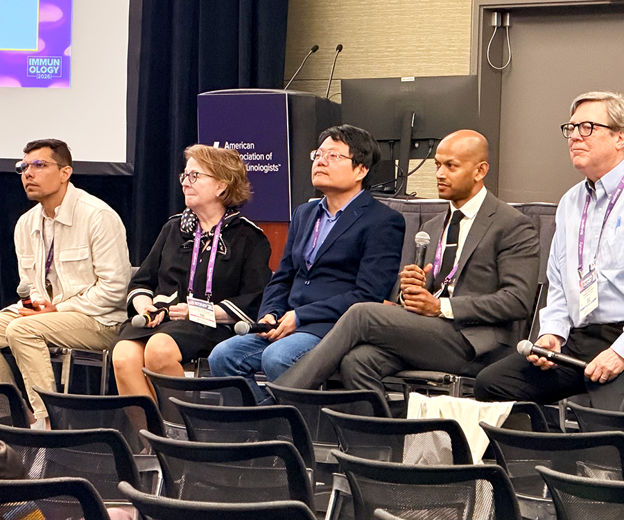 A group of four men and one woman sit at the front of a room during a panel discussion.