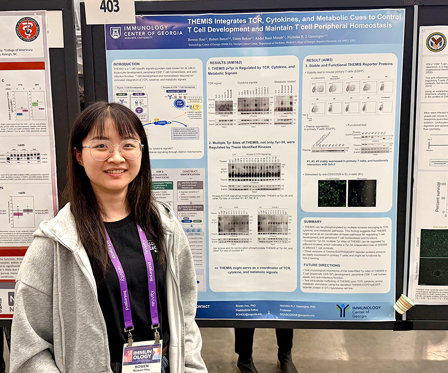 A woman stands beside her scientific poster during a poster session at a large conference.