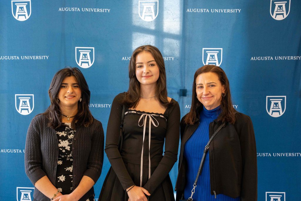 Two high school-aged girls smile beside an older woman.