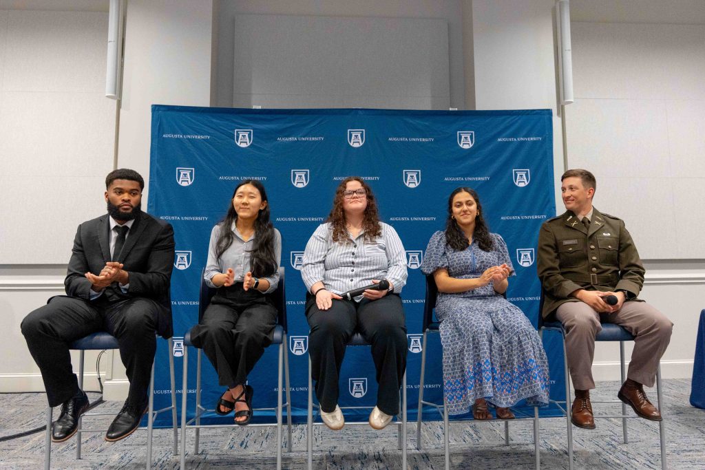 A line of four college-aged men and women lined up sitting in chairs.