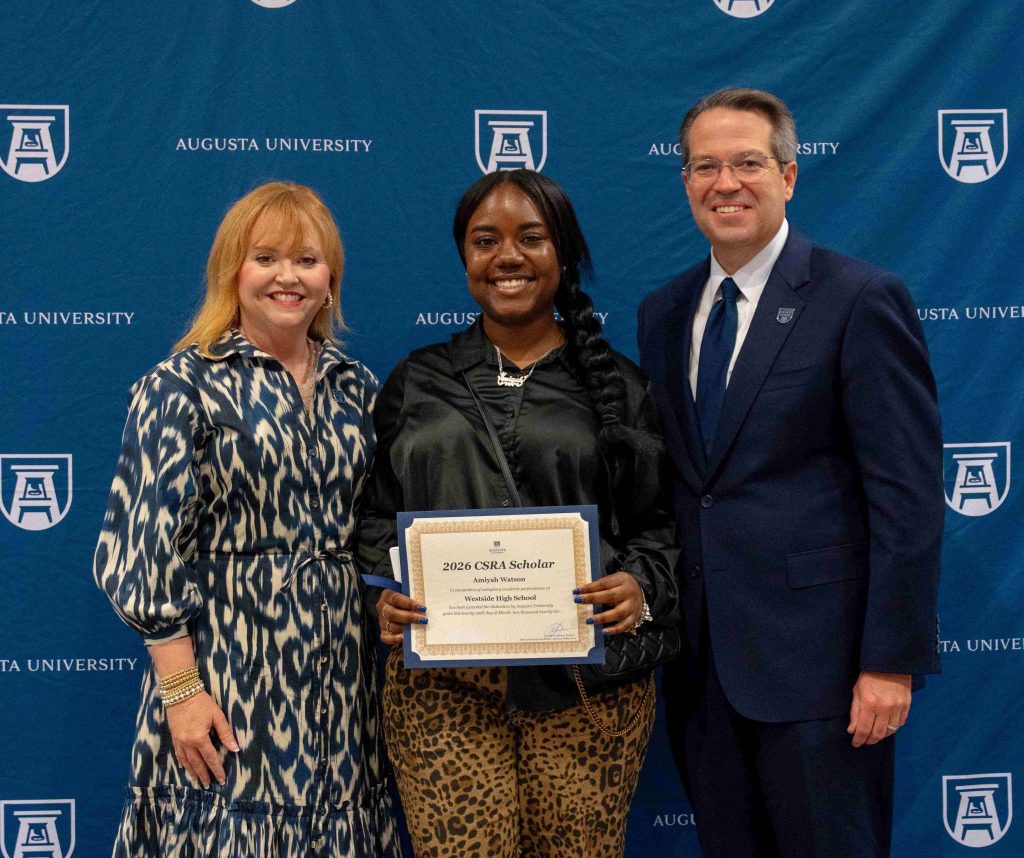 A  high school-aged girl holds a certificate smiling between an older man and woman.