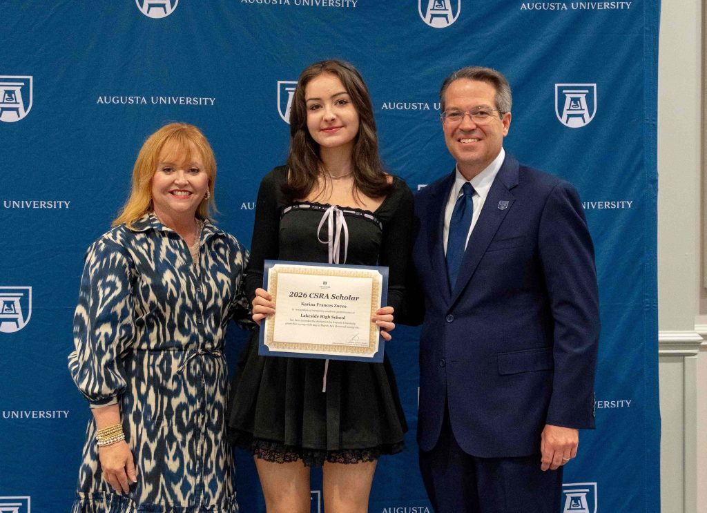 A high school-aged girl holds a certificate smiling between an older man and woman.