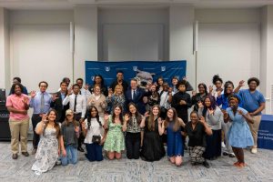 A large group of men and woman, in a addition to a jaguar mascot, pose for a photo.