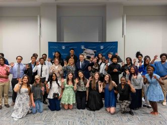 A large group of men and woman, in a addition to a jaguar mascot, pose for a photo.