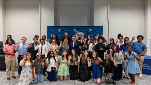 A large group of men and woman, in a addition to a jaguar mascot, pose for a photo.