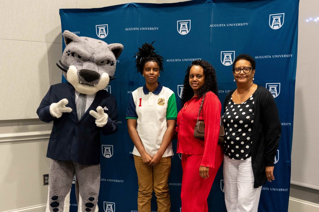 Three women pose for a photo with a jaguar mascot.