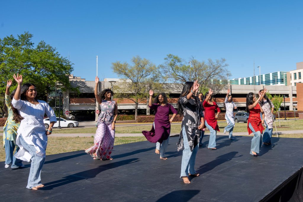 Women dressed in traditional Indian clothes dance on an outdoor stage.