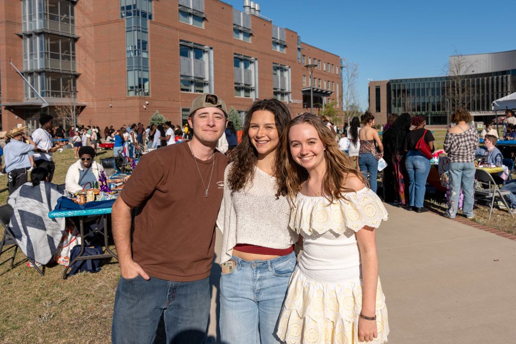 One man and two women pose for a photo, facing away from a large crowd in the background.