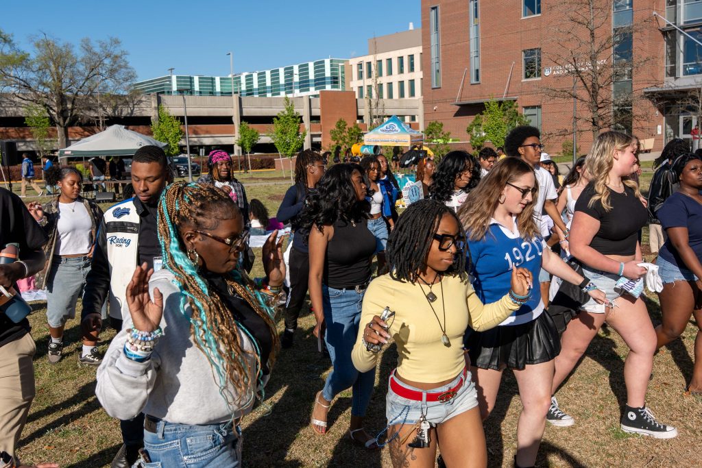 A large crowd of men and women dancing on an outdoor field.