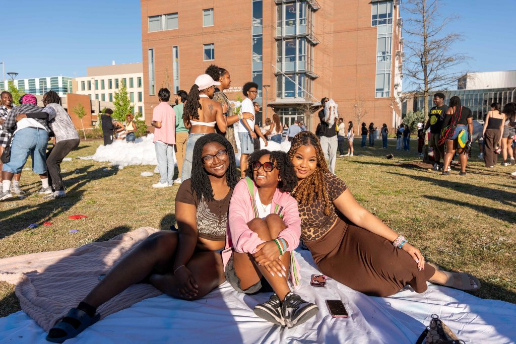 Three girls pose for a photo while sitting on a picnic blanket.