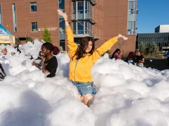 A girl poses with her arms up in the middle of a large amount of foam.