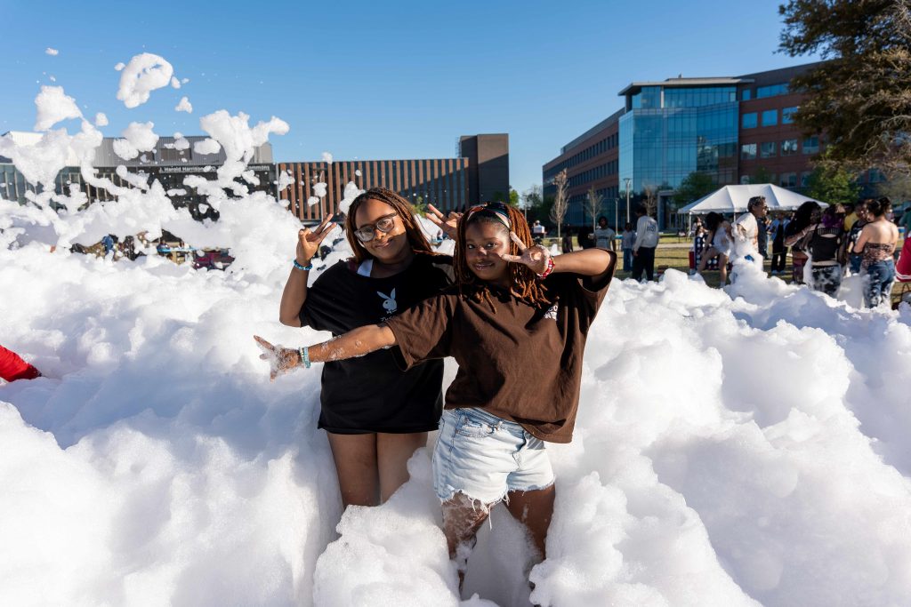 Two girls holding up peace signs pose for a photo while standing in a large amount of foam.