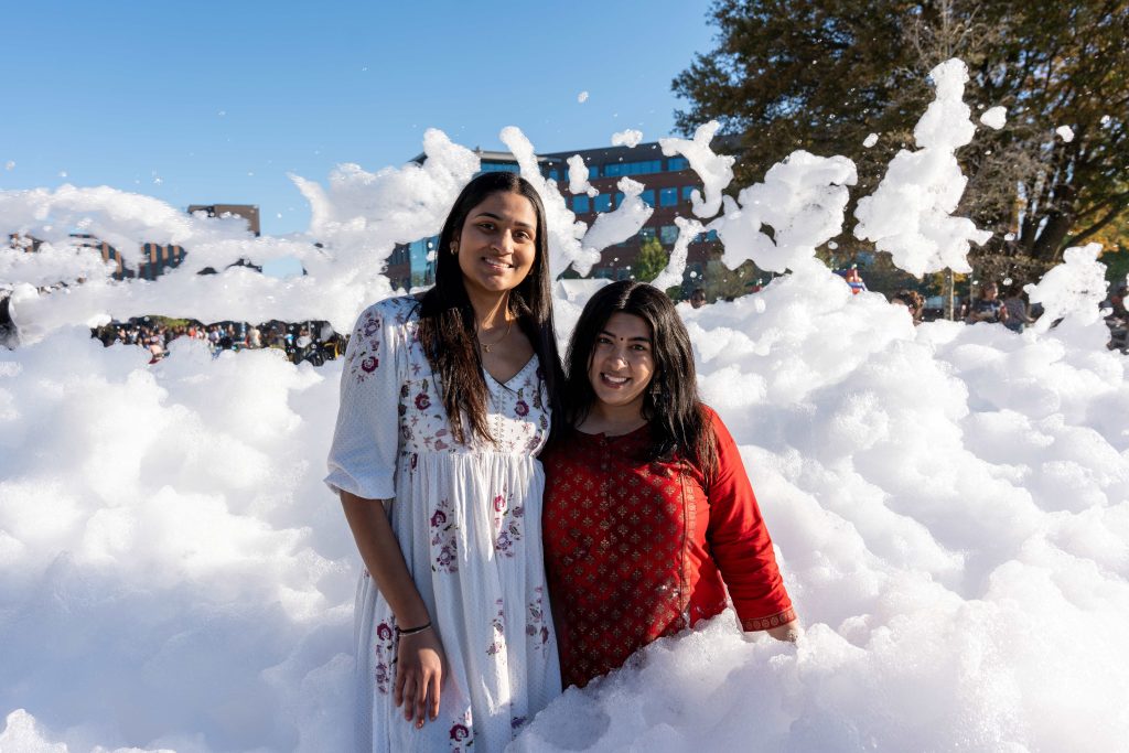 Two girls pose for a photo while standing in a large amount of foam.