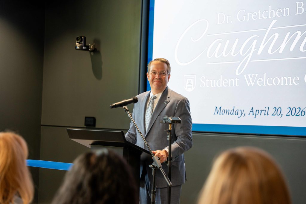 An older man wearing a suit smiling behind a podium. 