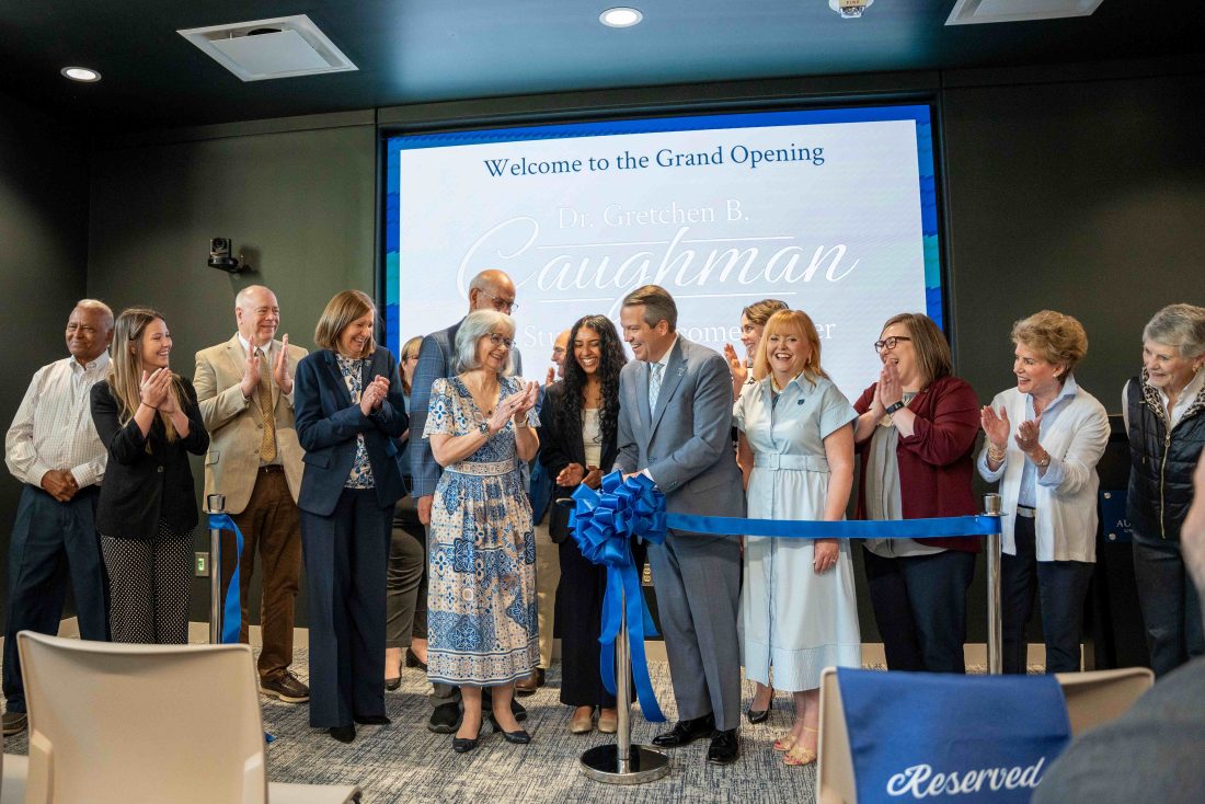 A large group of men and women gathered behind a ribbon at an indoor event.