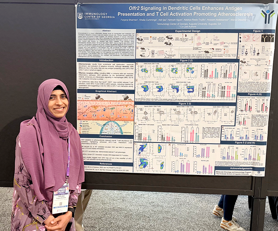 A woman stands beside her scientific poster during a poster session at a large conference.