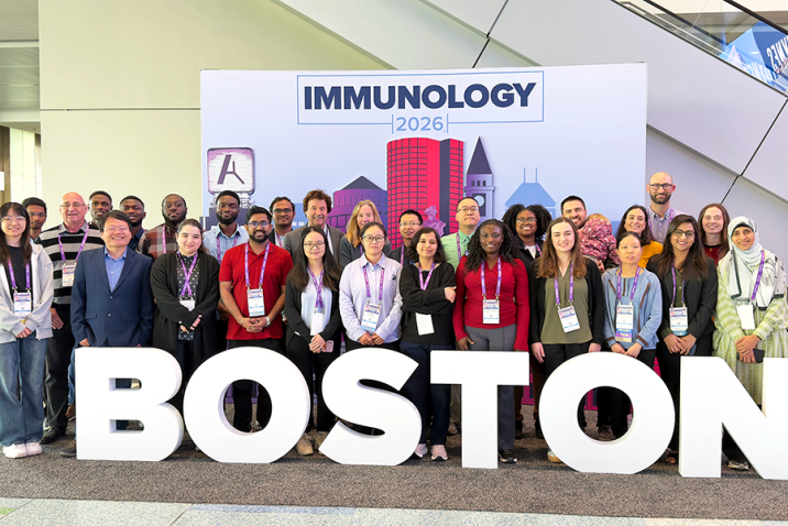 A group of 28 people stand in a photo booth that includes oversized letters spelling out 