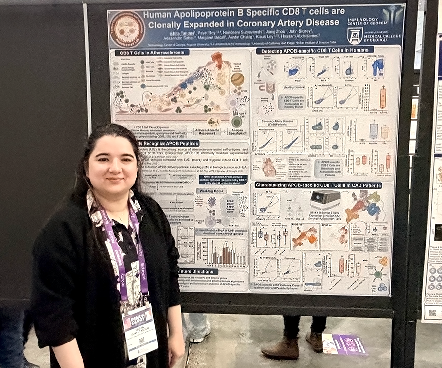 A woman stands beside her scientific poster during a poster session at a large conference.