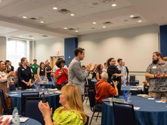 Men and women clapping while standing in between several tables.