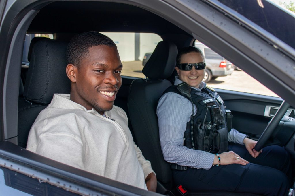 A young college-aged boy and older police officer sitting in an Augusta University police car.