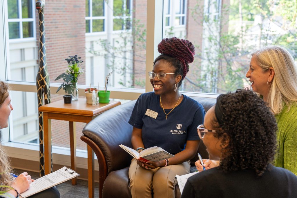 Several women listening to a college-aged girl who is holding a book.