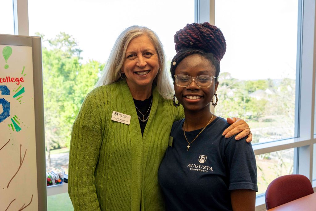 An older woman with her arm placed around a young college-aged girl.