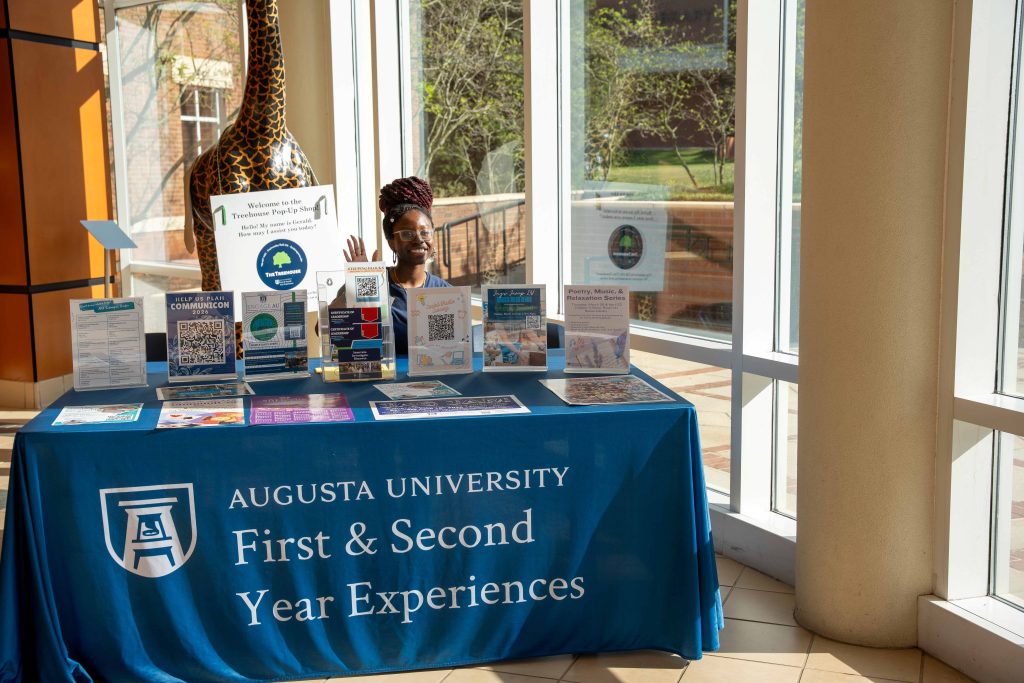 A college-aged girl sitting behind a table that has several paper resources on it.