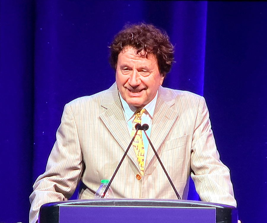 A man stands at a podium and gives a scientific presentation to a large group of people.