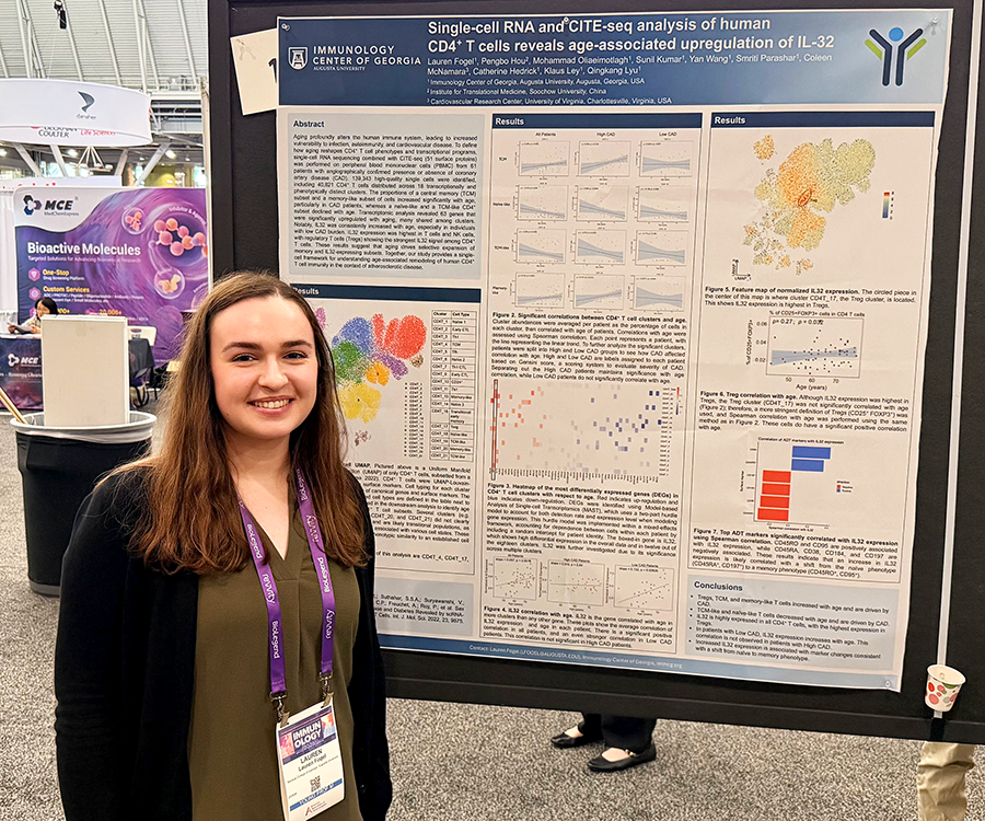 A woman stands beside her scientific poster during a poster session at a large conference.