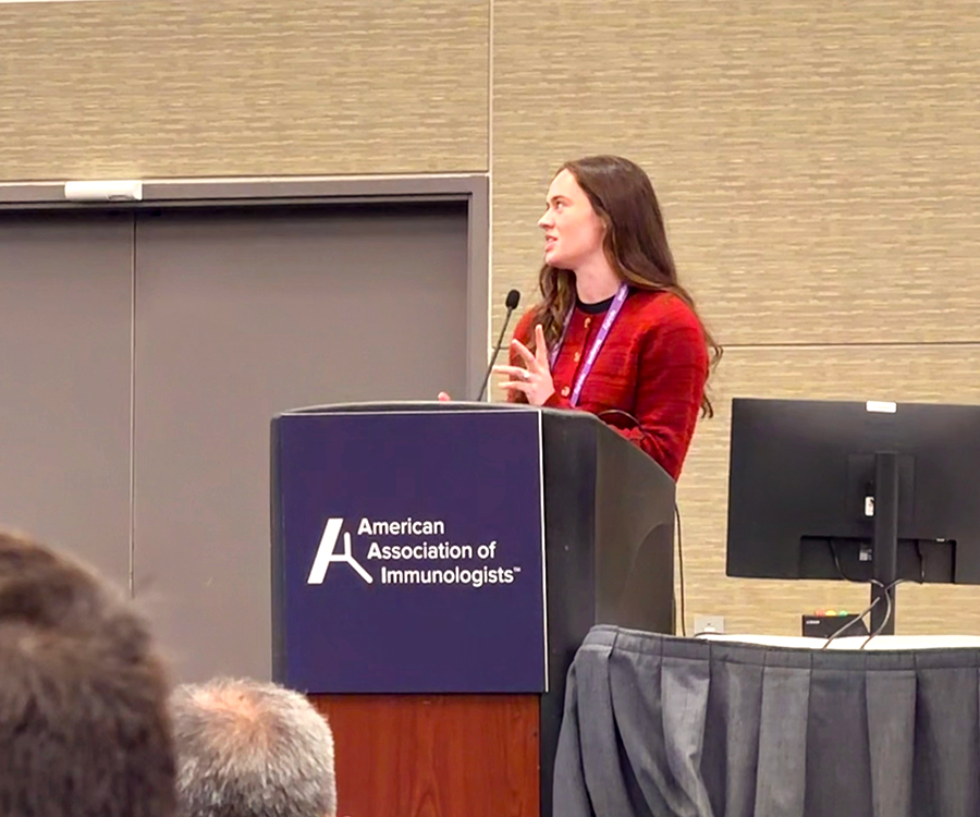 A woman stands at a podium and gives a scientific presentation to a large group of people.