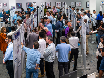 Many people gather around large posters in a room.