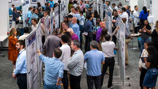 Many people gather around large posters in a room.
