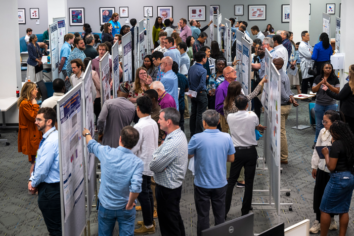 Many people gather around large posters in a room.