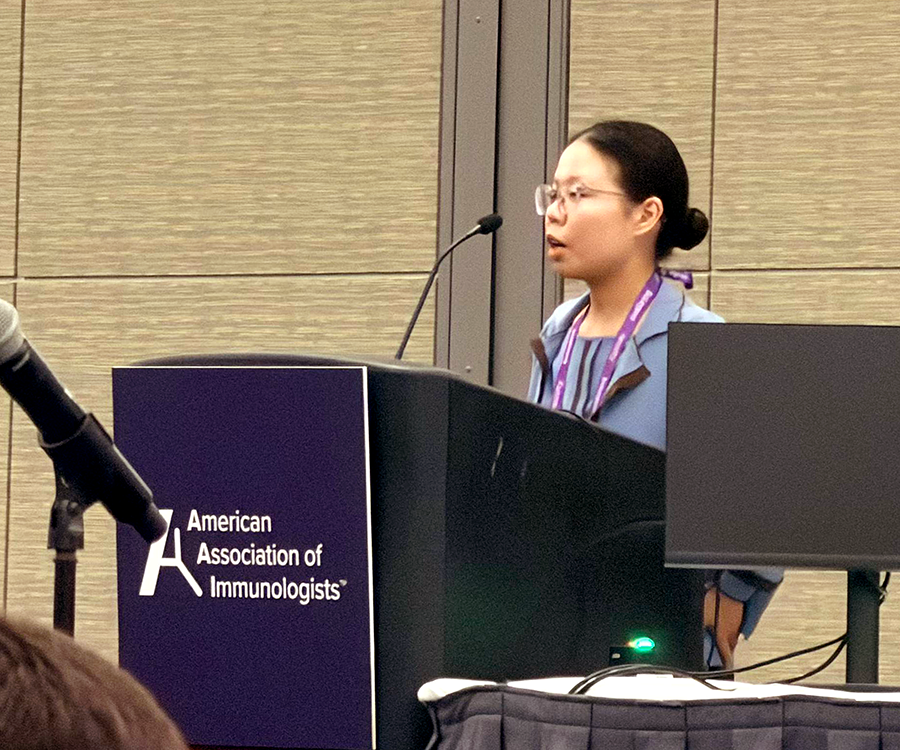 A woman stands at a podium and gives a scientific presentation to a large group of people.