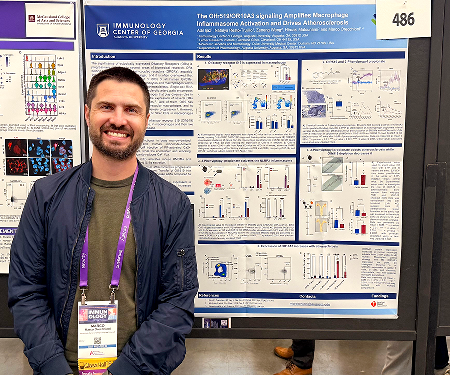 A man stands beside his scientific poster during a poster session at a large conference.