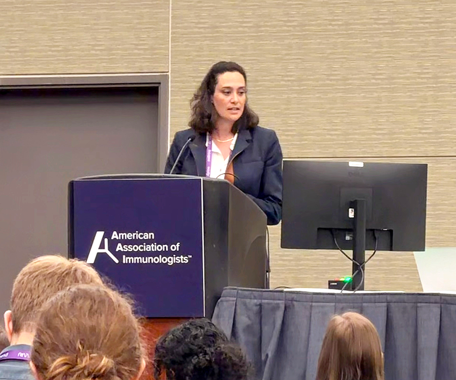 A woman stands at a podium and gives a scientific presentation to a large group of people.