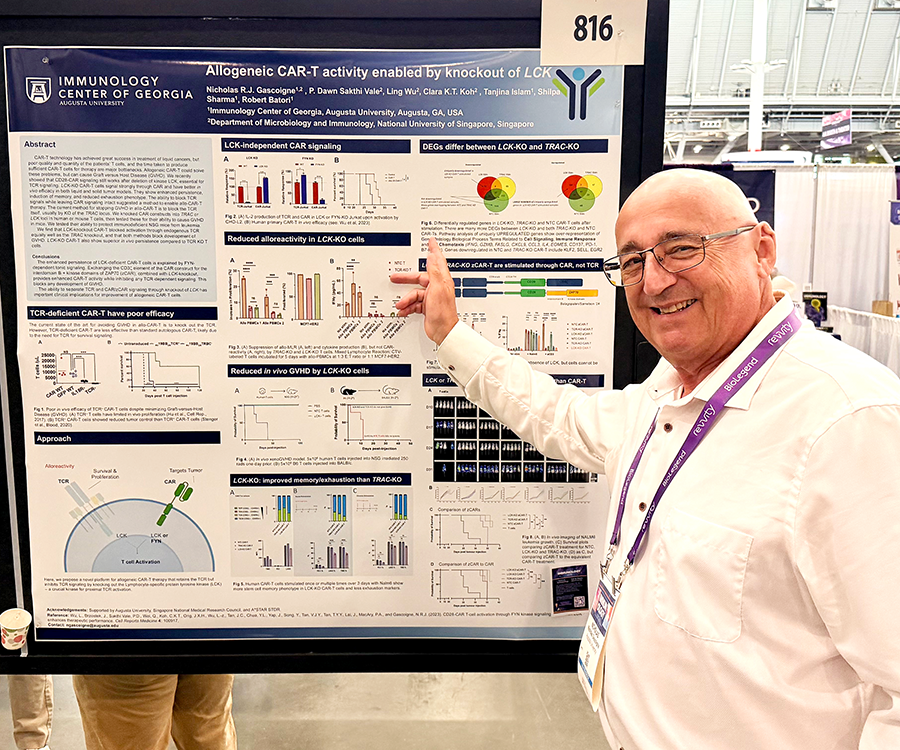 A man stands beside his scientific poster during a poster session at a large conference.