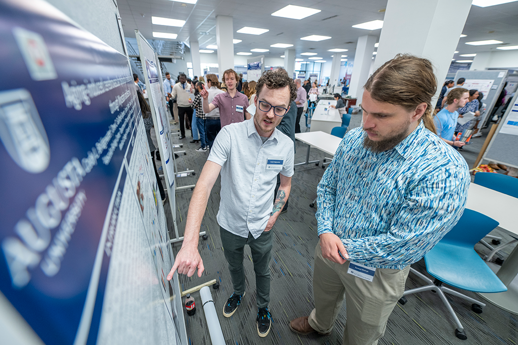 Two men point and look at a large board.