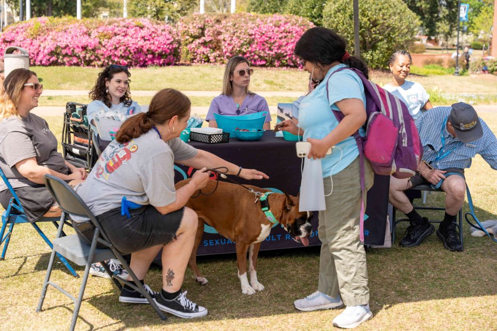 Several men and women sit around a table while a college-aged woman pets a dog nearby.