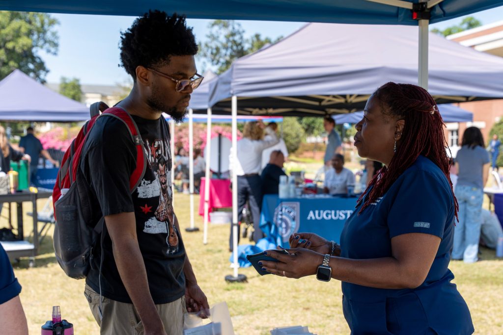 At an outdoor tabling event, a college-aged man speaks with a tabling assistant.